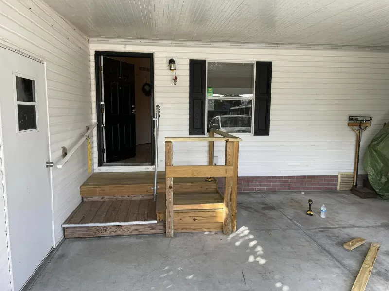 A house porch with a new wood landing and a partial railing, a drill lying on the deck.
