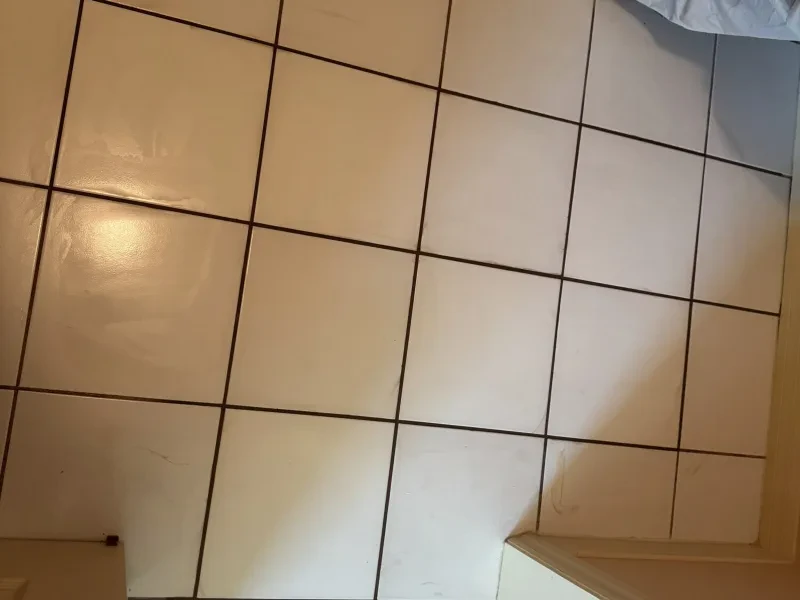 The same white tile floor, clean, with the cabinet edge still at the lower right.