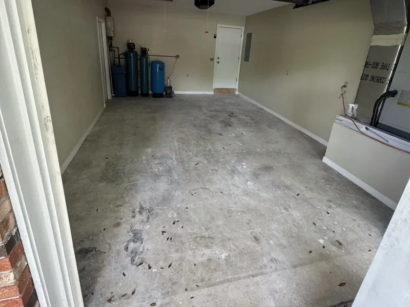 A bare gray concrete garage floor, with blue water-softener tanks along the left wall.