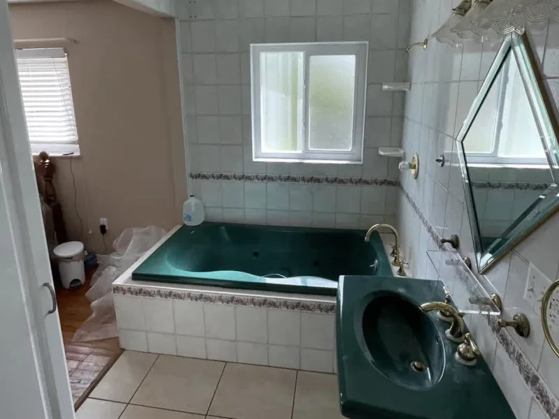 A bathroom with a dark green jetted tub, a green sink, and a gold-framed diamond mirror.