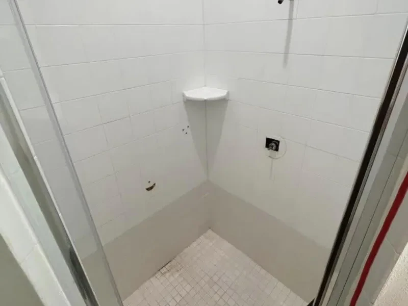 A small shower corner in white subway tile, with one corner shelf and an open valve hole.