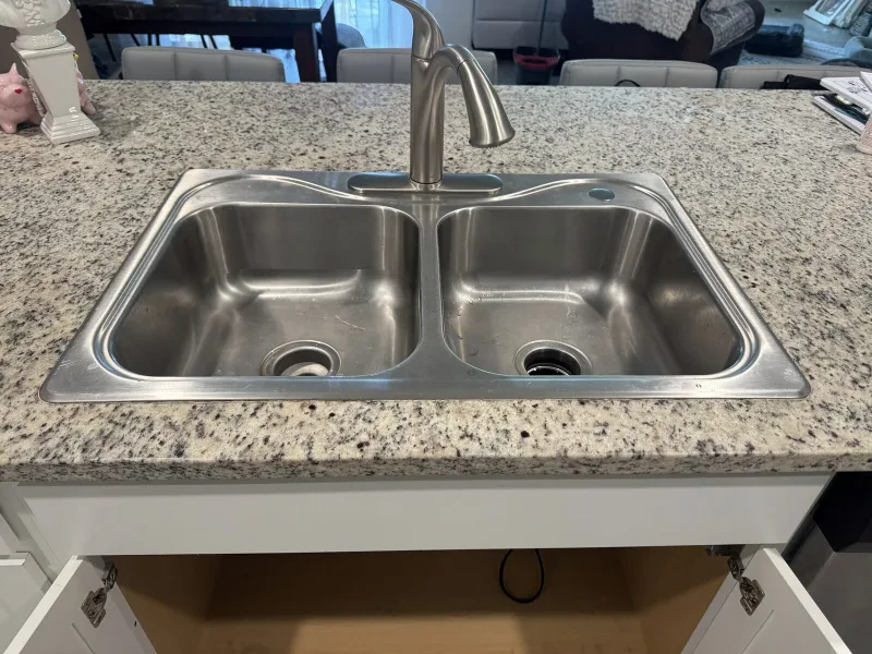 A stainless double-bowl kitchen sink and a stainless faucet set in a speckled granite counter.