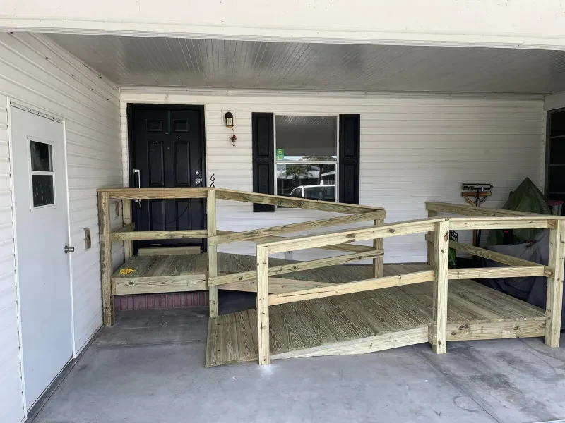 A pressure-treated wooden wheelchair ramp with railings, built onto a house porch.