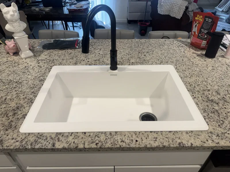 A white single-bowl kitchen sink and a matte black faucet in the same granite counter.