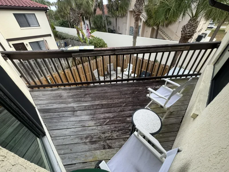 A weathered gray wood deck and railing on a condo balcony, seen from above.