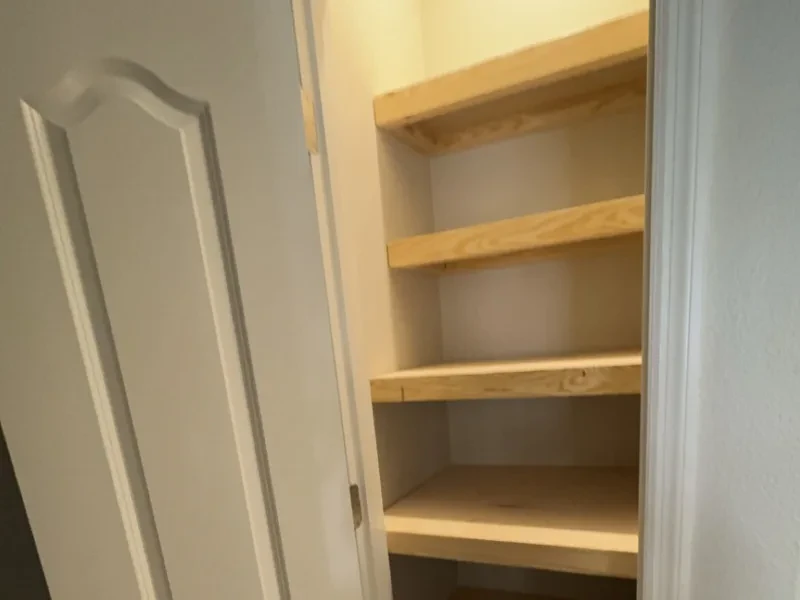 An open closet with pine shelves, beside a white door.