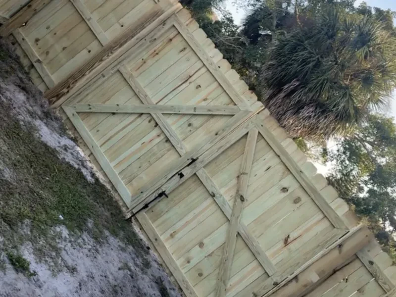 Two light-wood fence gates, each with an X brace, and a palm behind the fence.