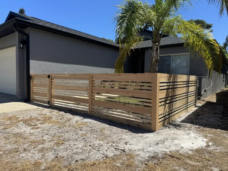 A light cedar horizontal-slat fence and gate in front of a gray house.
