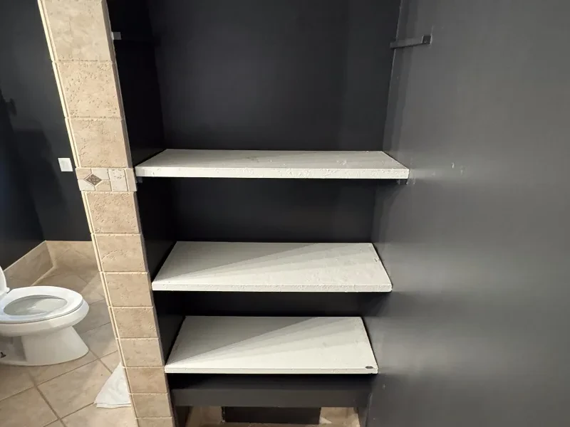A bathroom niche with three white shelf boards beside a beige tile column.